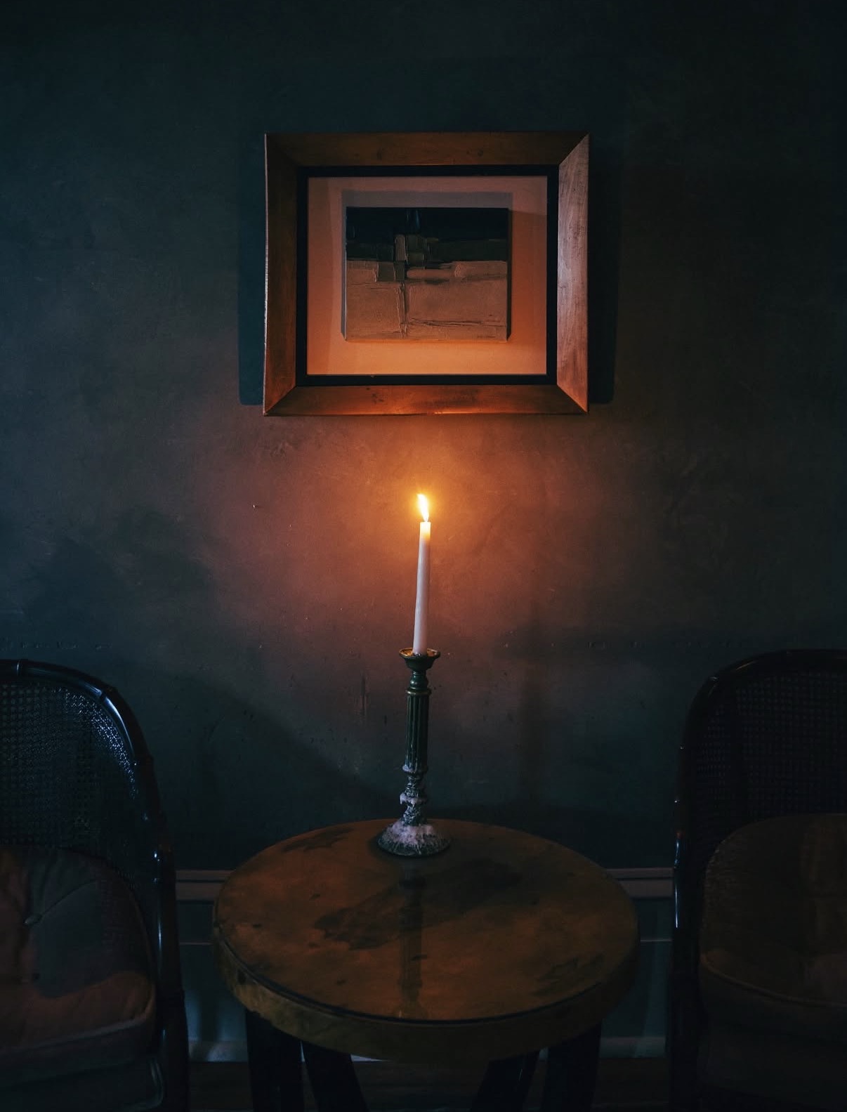 A single taper candle burning on a café table against a dark wall